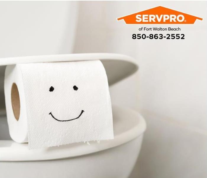 Toilet paper with a happy face drawn on it sits on a toilet seat.